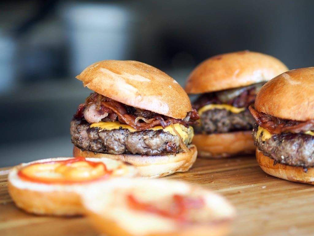 A row of bacon cheeseburgers on a board